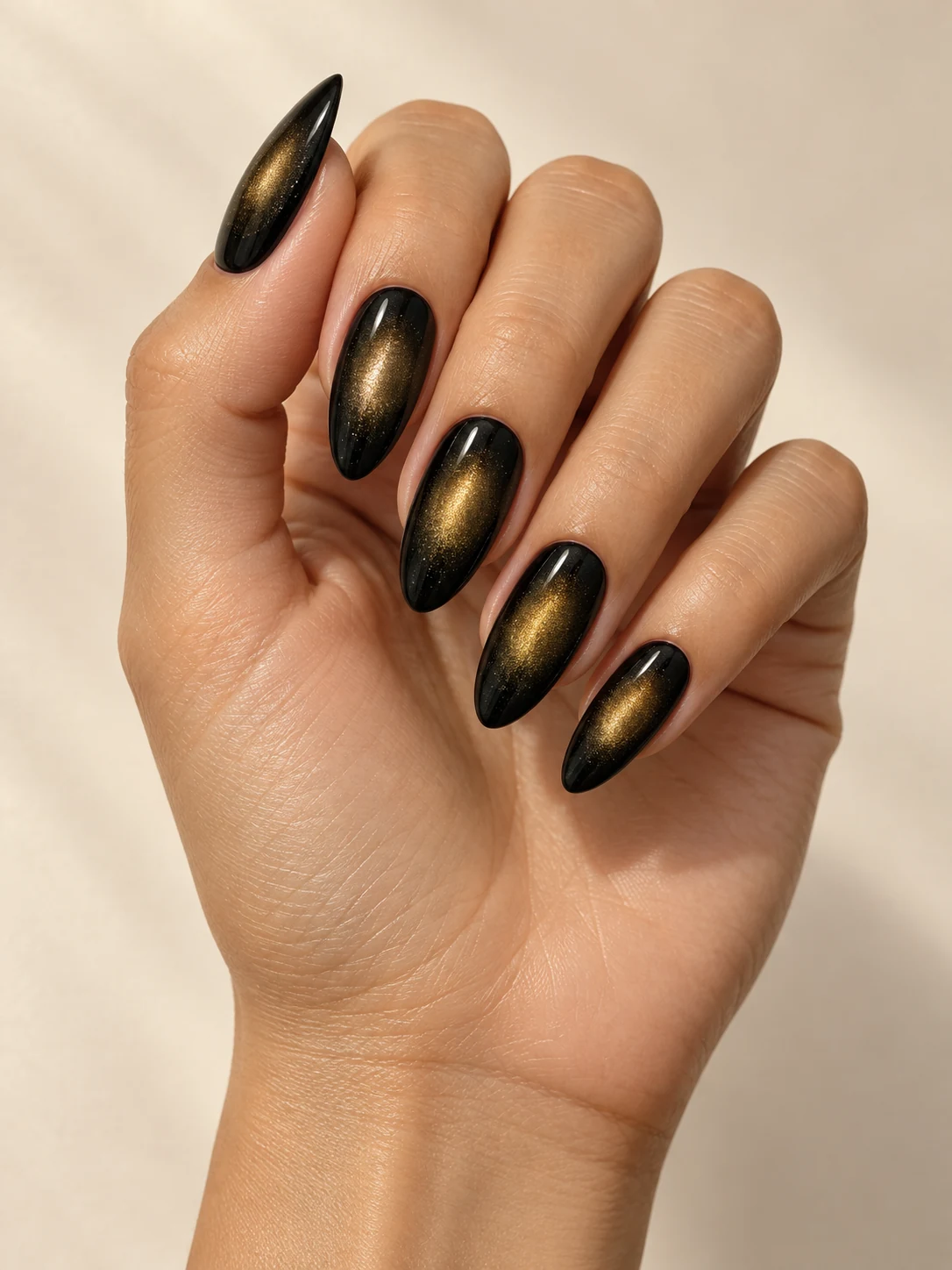 Deep black nails with a soft oval golden magnetic halo glowing at the center of each nail, no gems on light golden skin; long almond manicure.