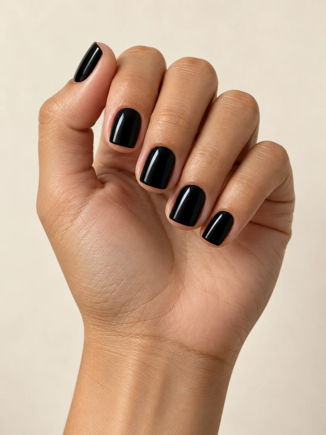 Compact perfectly straight square nails coated in rich glossy jet black, crisp clean outlines and no decorations on warm medium skin; short square manicure.