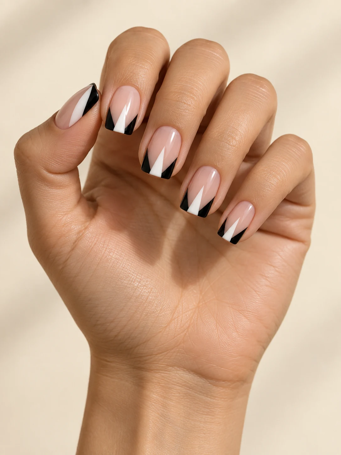 Nude square nails with a narrow white central triangle flanked by black side panels at the free edge, elegant tuxedo geometry on light golden skin; medium square manicure.