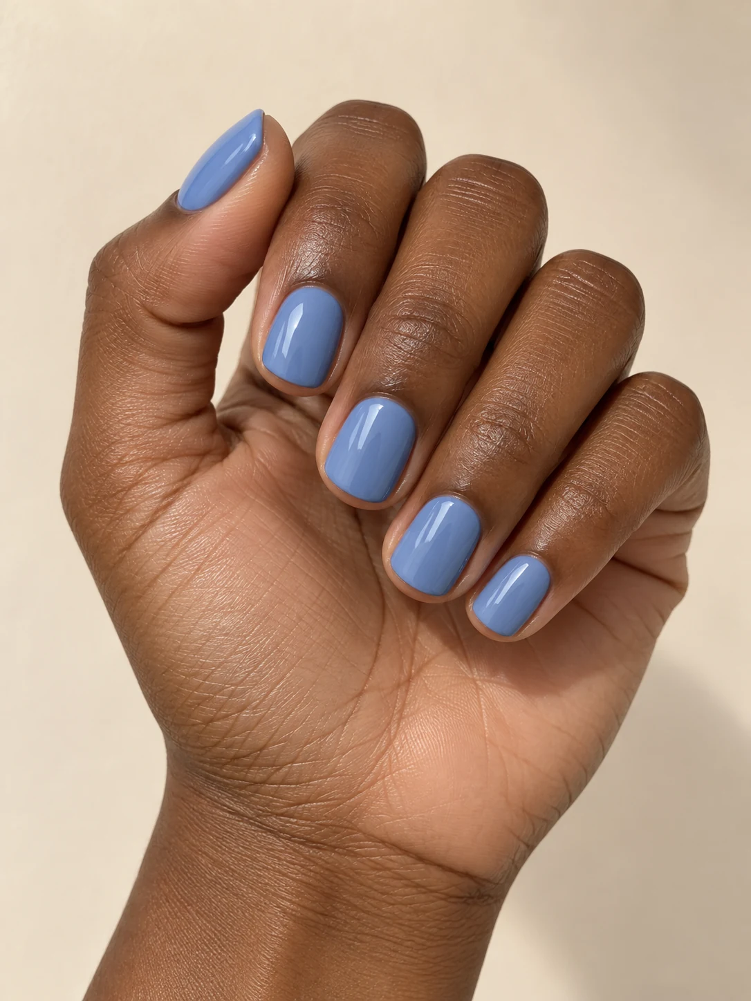 Creamy pastel blueberry-blue short squoval nails with smooth opaque gloss and neat compact edges on rich deep brown skin; short squoval manicure.