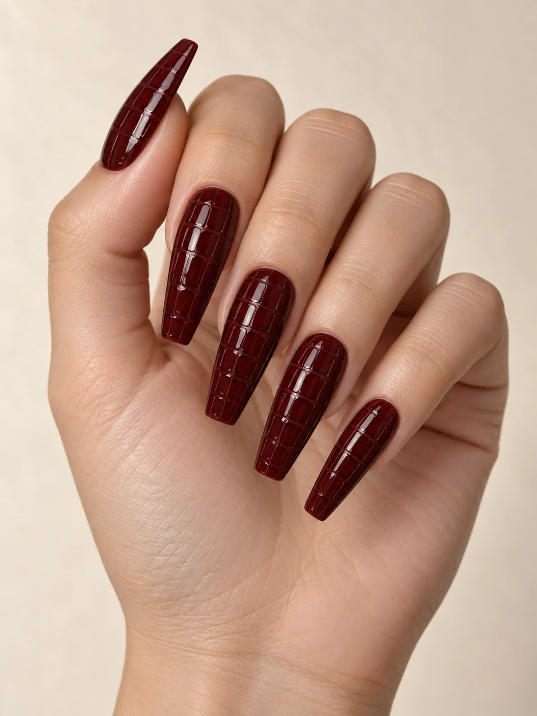 Deep burgundy coffin nails with a subtle tonal crocodile-grid pattern made of slightly darker glossy lines, no raised spikes on fair neutral skin; long coffin manicure.