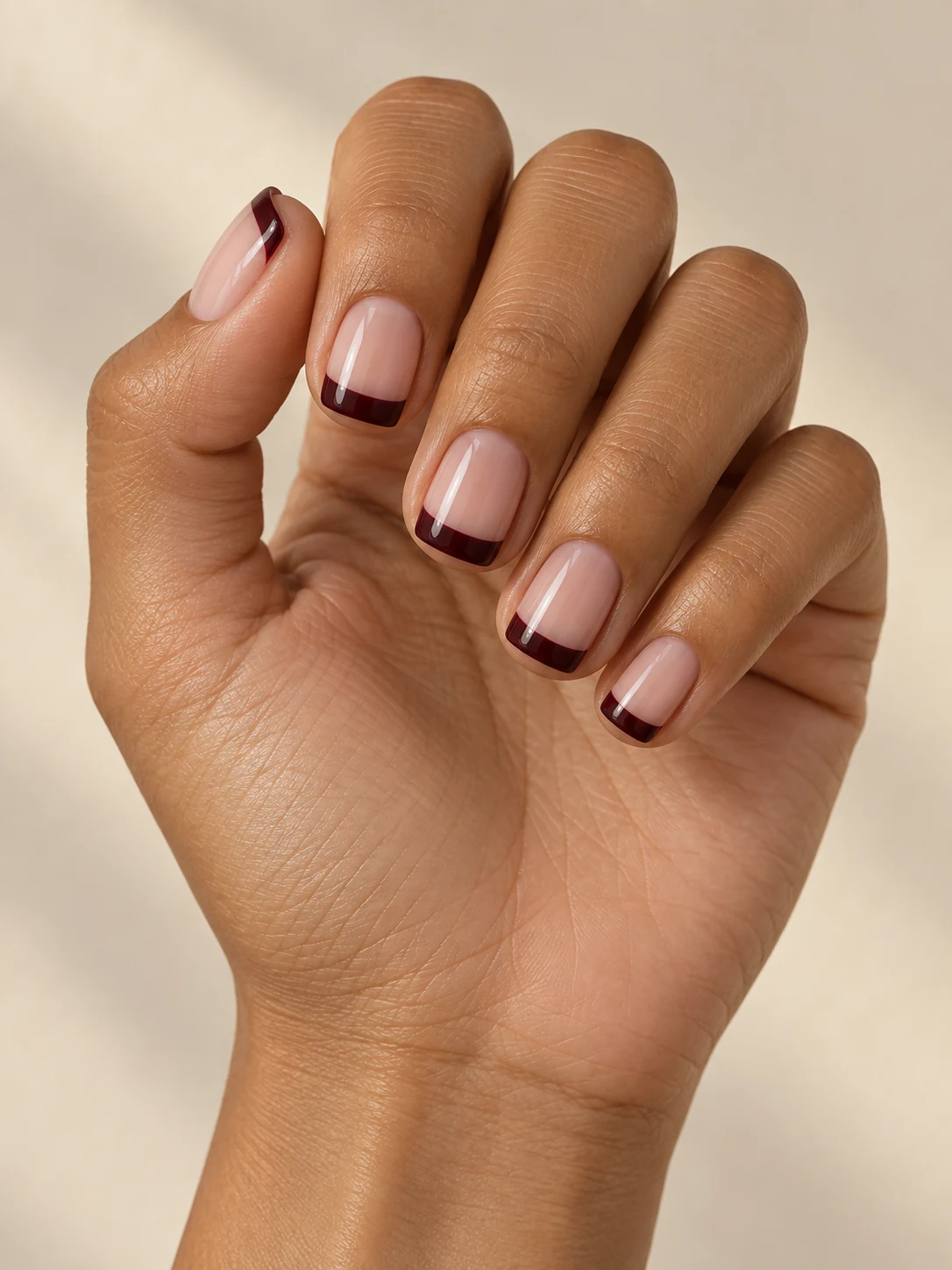 Short square sheer nude nails with straight deep burgundy tips and crisp clean corners on olive tan skin; short square manicure.