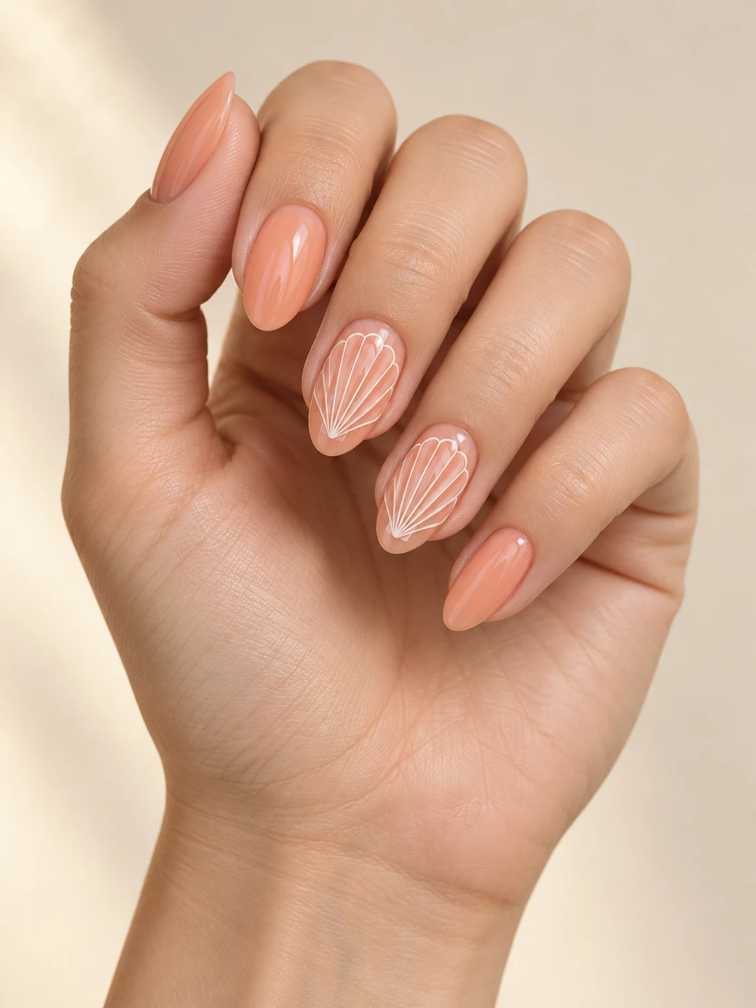 Sheer peach-coral nails with fine white fan-like seashell lines on two accent nails, flat elegant coastal drawing on fair neutral skin; medium almond manicure.