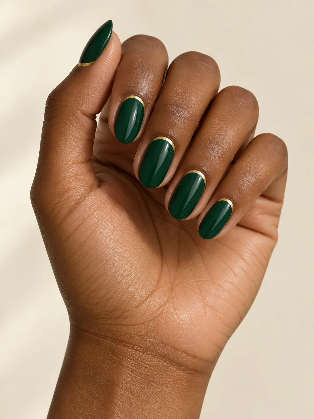 Opaque deep emerald oval nails with a narrow gold outline following only the cuticle curve on deep warm brown skin; medium oval manicure.