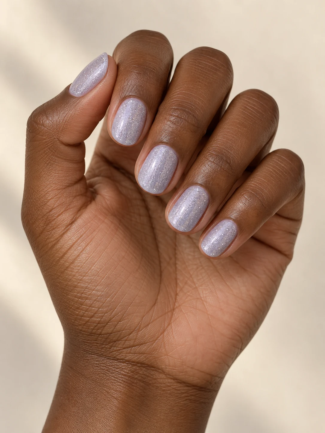 Pale icy lilac short oval nails with an evenly scattered ultra-fine silver shimmer, delicate winter frost effect on rich deep brown skin; short oval manicure.