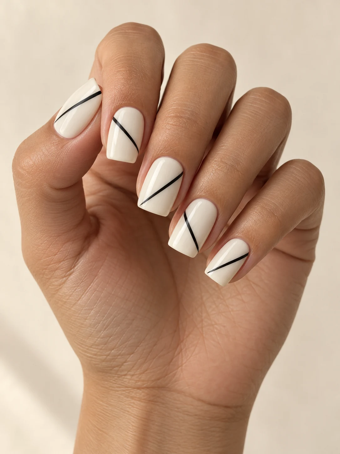 Creamy ivory nails with one thin black diagonal brushstroke across each surface, alternating the stroke direction subtly on warm medium skin; medium square manicure.