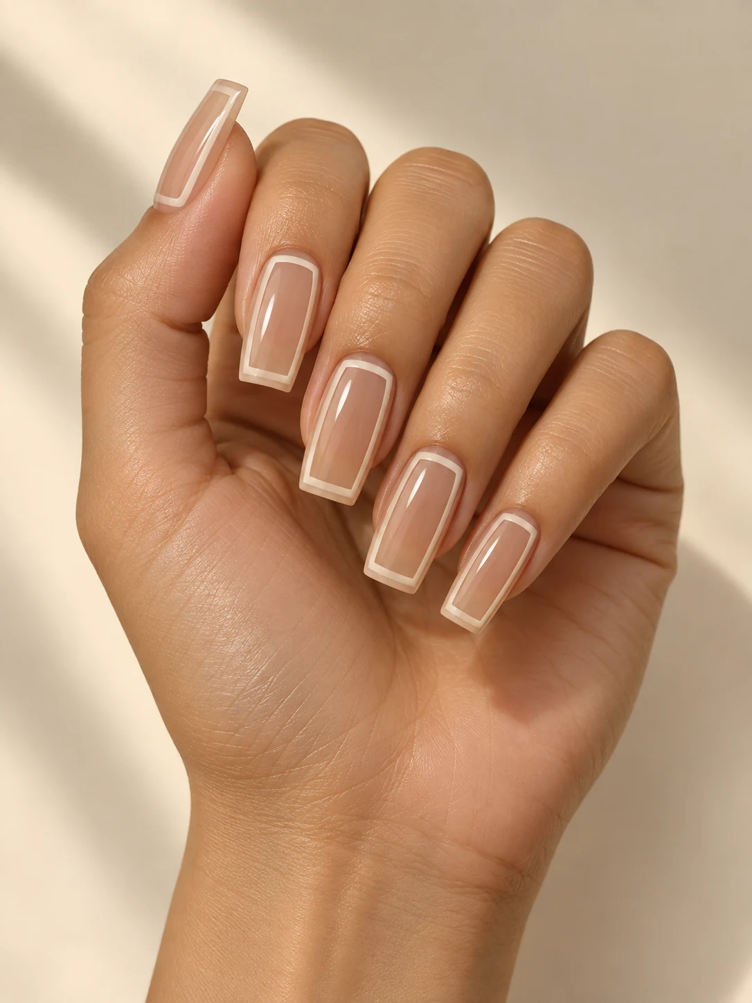 Sheer beige long square nails with a thin ivory rectangular frame inset from the edges, transparent center on light golden skin; long square manicure.