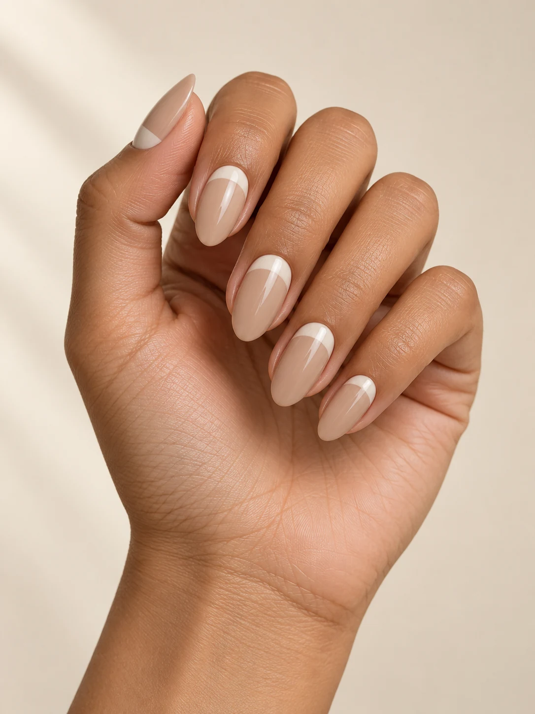 Soft beige nails with a clean opaque ivory crescent following the cuticle, the free edges remaining beige on warm medium skin; medium almond manicure.