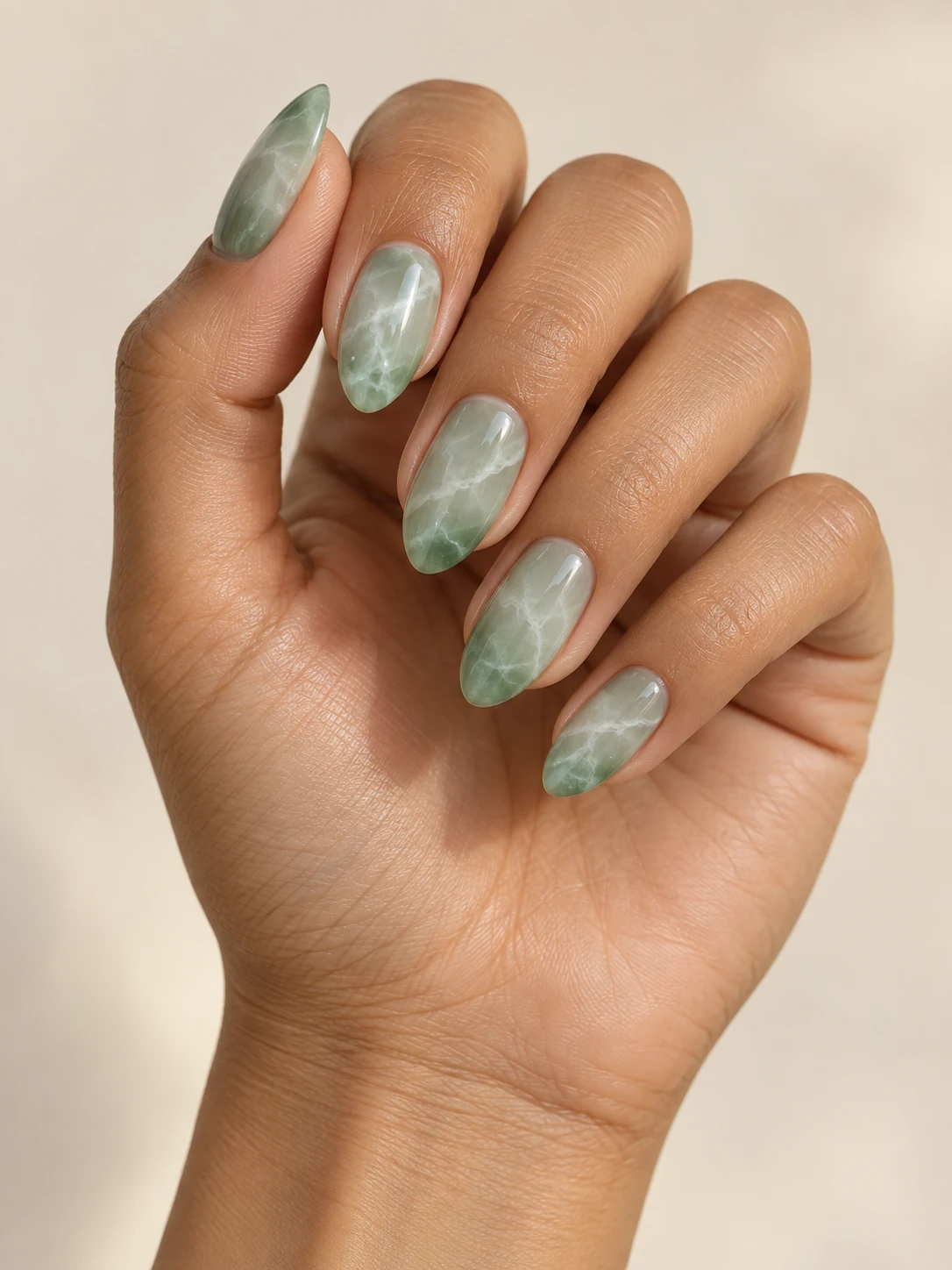 Translucent pale jade nails with fine cloudy white stone-like veining, slightly deeper green edges and smooth glossy finish on warm medium skin; medium almond manicure.