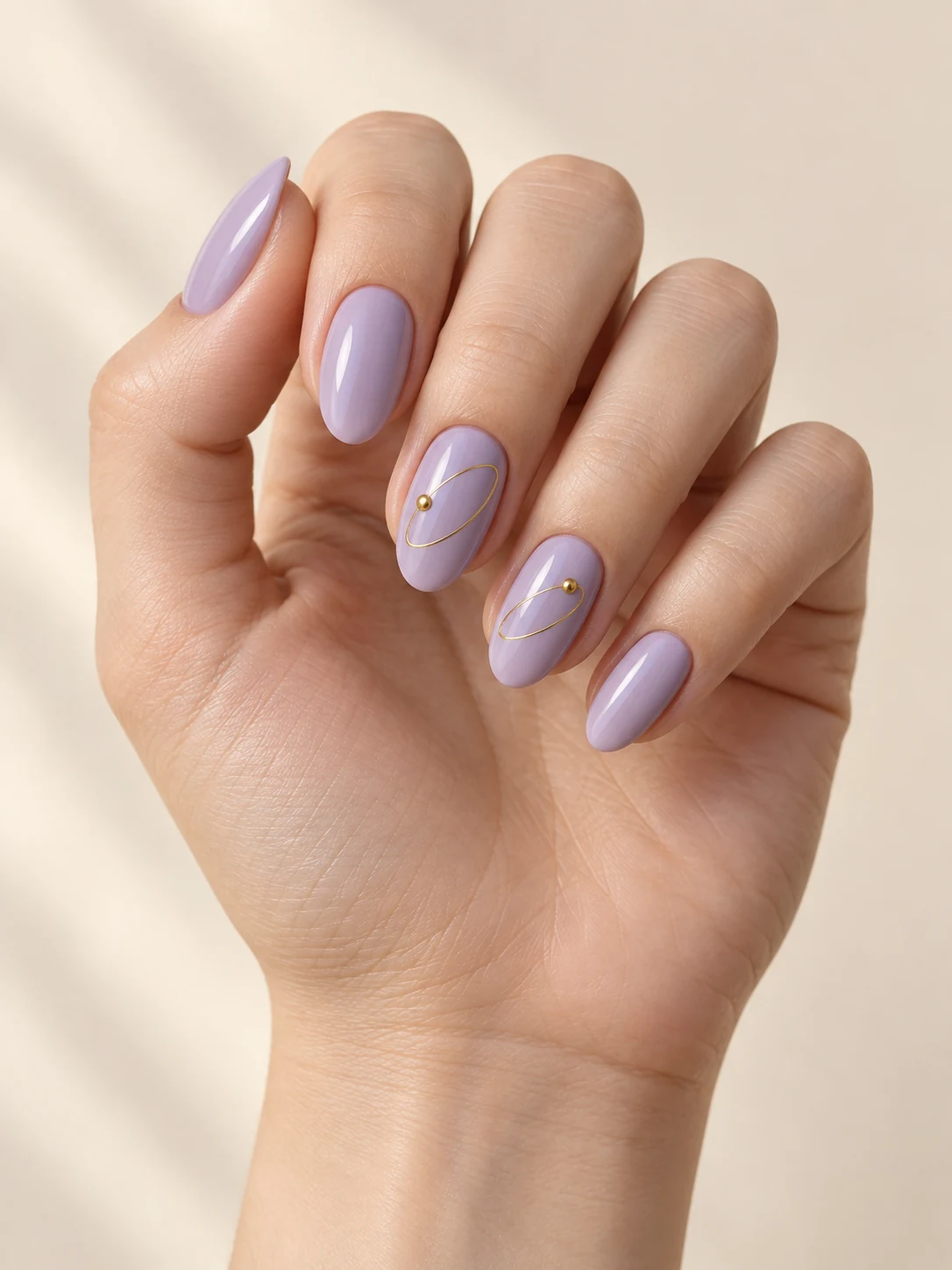 Pale lavender nails with one thin elliptical gold orbit line and one tiny gold dot on two accent nails on fair neutral skin; medium oval manicure.
