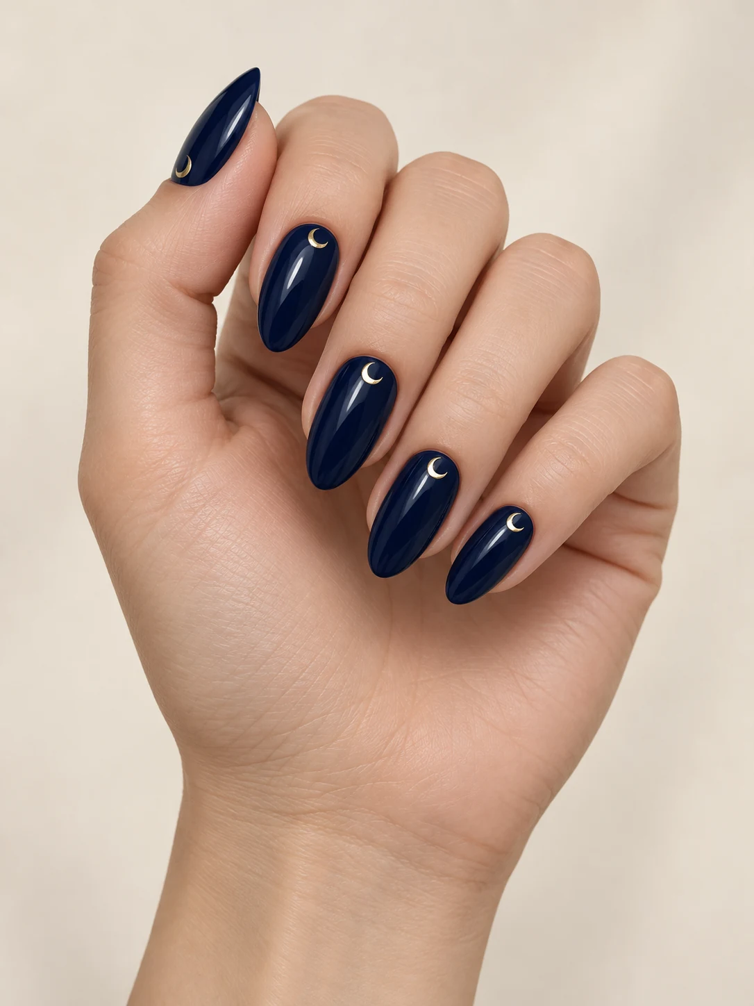 Deep glossy navy nails with one tiny gold crescent moon near each cuticle and no star pattern on fair neutral skin; medium almond manicure.