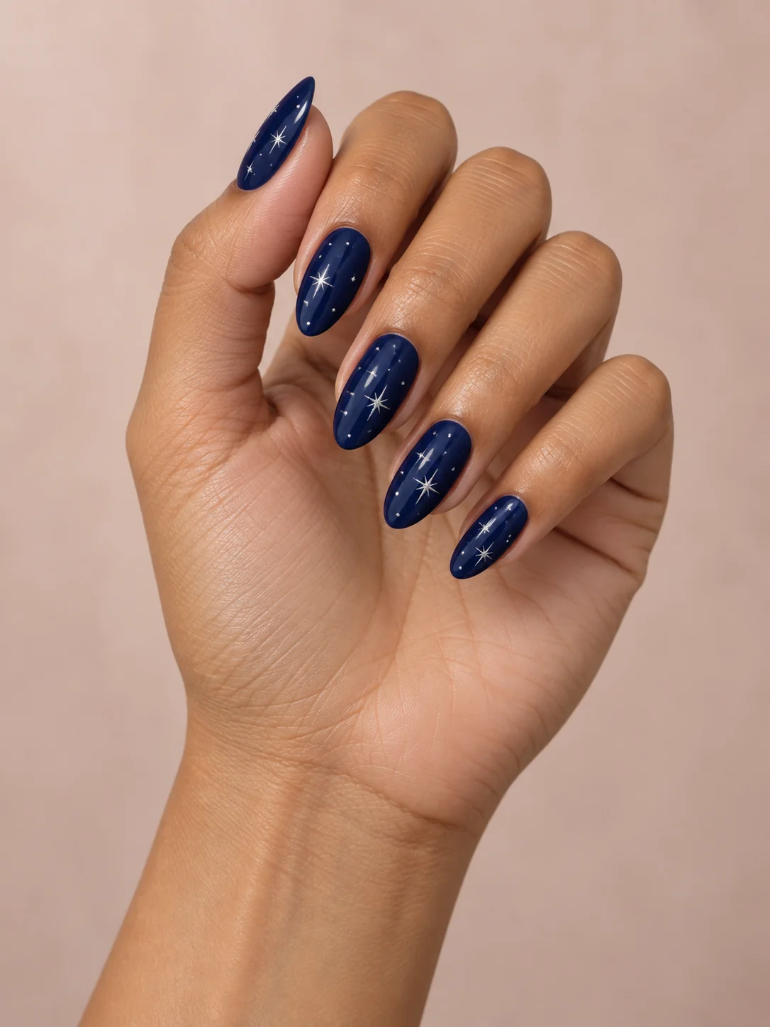Tiny silver stars sit against a glossy navy-blue base on almond nails.
