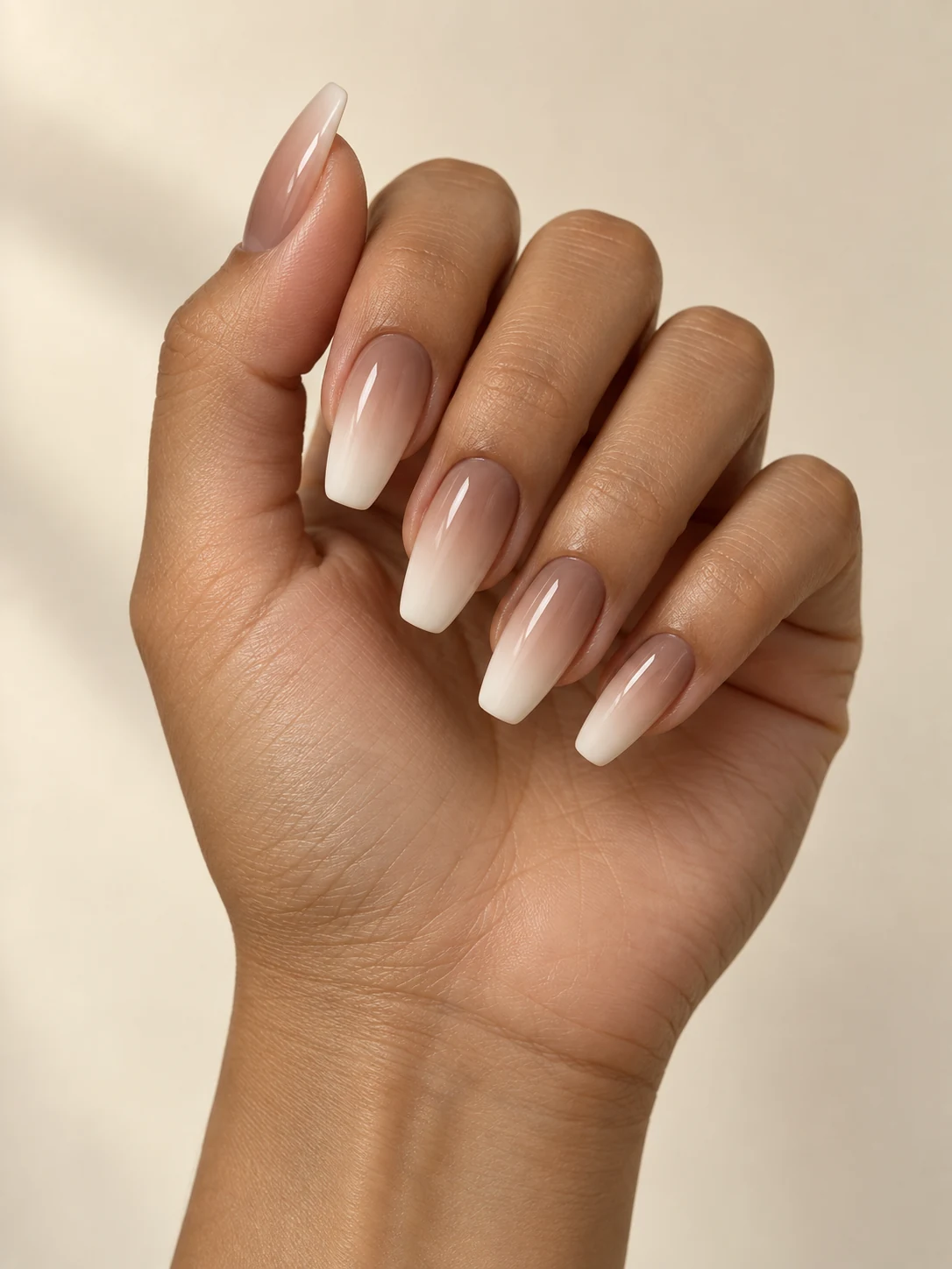 Milky mocha nails fading seamlessly into soft ivory free edges, a restrained warm neutral baby-boomer gradient on olive tan skin; medium coffin manicure.
