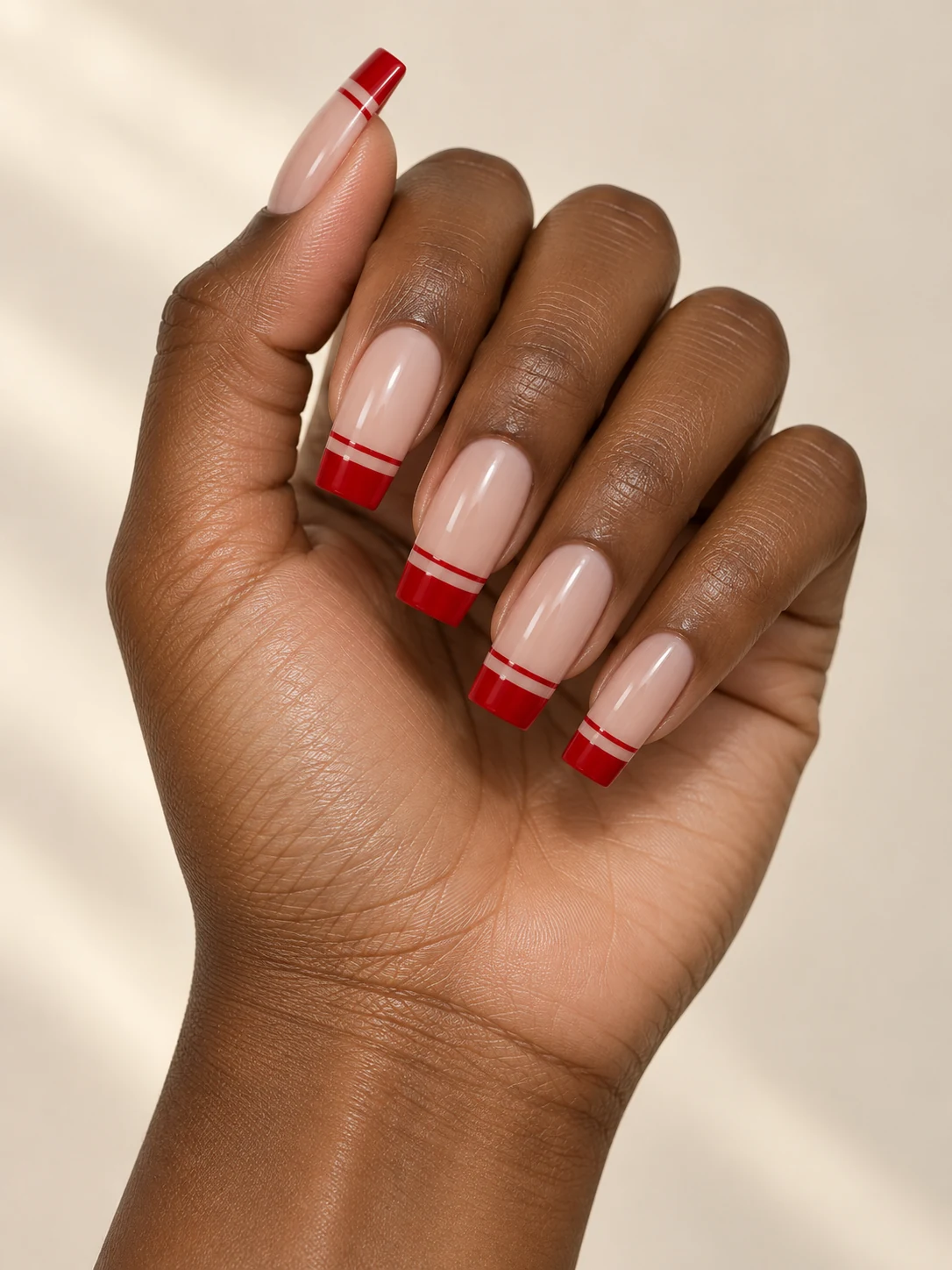 Long nude square nails with a crisp red French tip and a separate thin parallel red line directly below the tip on rich deep brown skin; long square manicure.