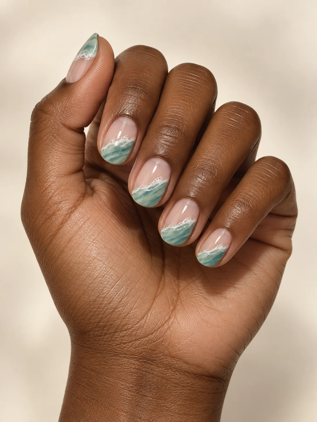 Nude oval nails with soft seafoam-green waves and a thin white foam line diagonally across the tips on deep warm brown skin; short oval manicure.