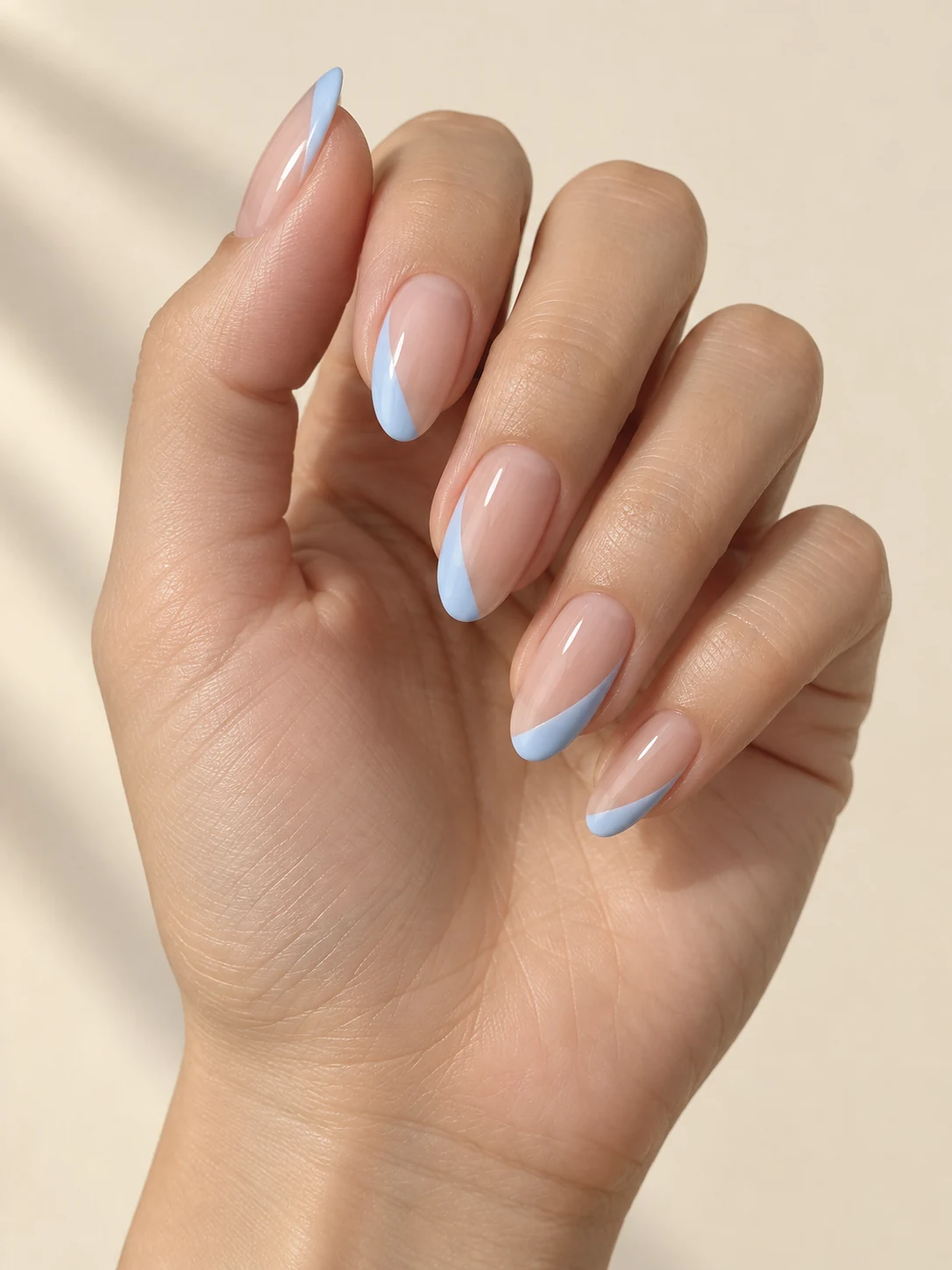 Clear nude nails with pastel sky-blue slivers on alternate sides of each almond tip, asymmetrical and delicate on fair neutral skin; medium almond manicure.