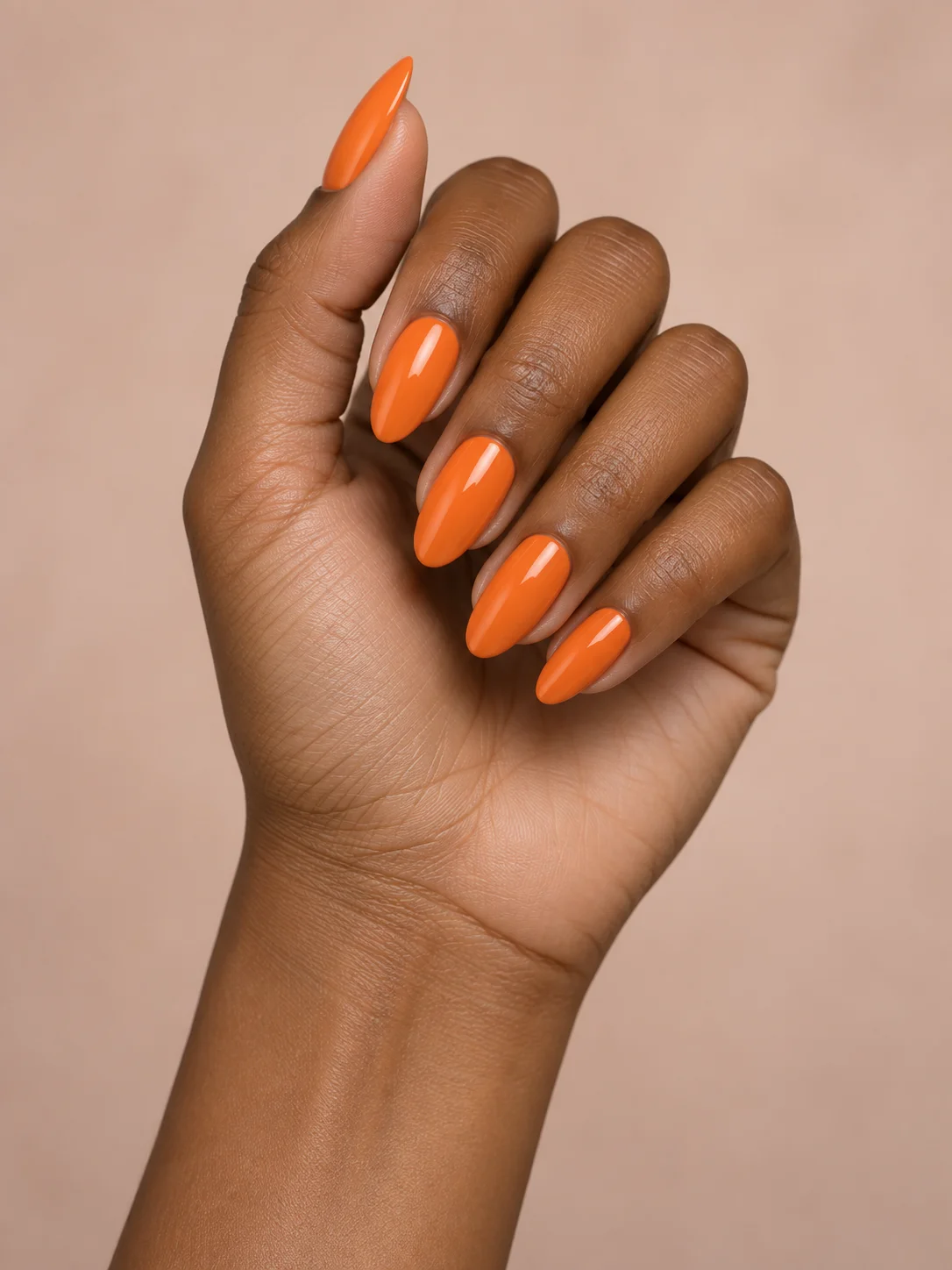 Juicy tangerine orange covers medium almond nails in a glossy, opaque finish.