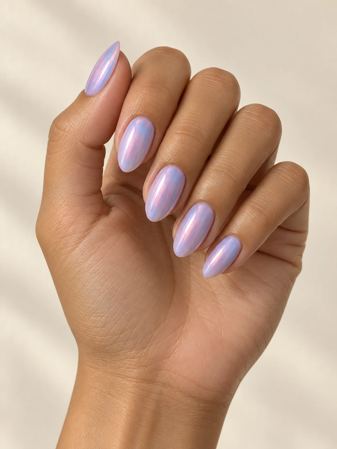 Pale lavender nails with a delicate opalescent pink-blue shift, luminous glossy surfaces without chunky glitter on olive tan skin; medium almond manicure.