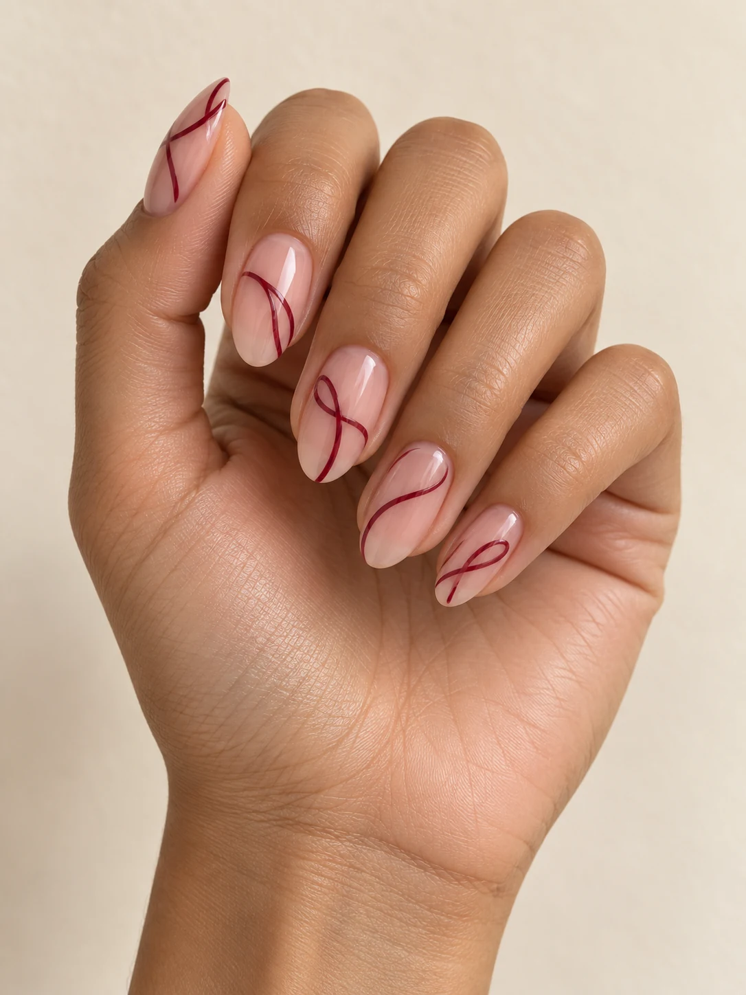 Transparent pink-nude nails with flowing fine wine-red ribbons looping once across each nail, sparse fluid lines on warm medium skin; medium oval manicure.